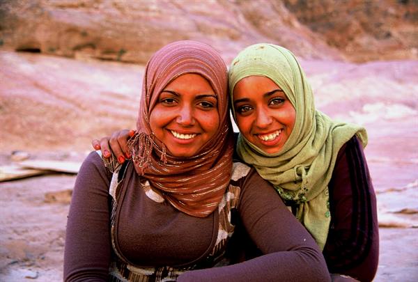 Two smiling young women in hijabs among the red rocks of Petra