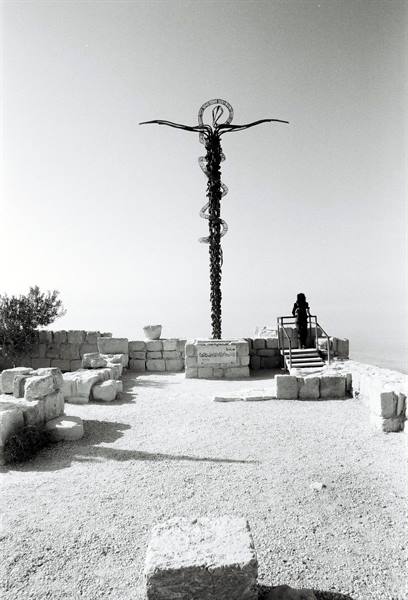 Metal cross with bronze serpent on Mount Nebo, ancient stones, a visitor stands