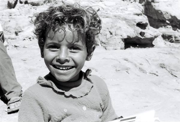 Smiling curly-haired child among desert rocks, black and white photo