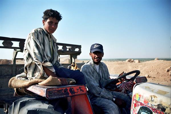 Two young men on a worn red tractor amid dry sandy fields