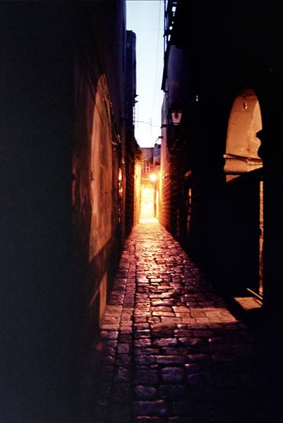 Narrow dark stone alley lit by warm orange light, arched walls