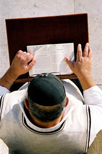Man wearing black kippah prays, reading a Hebrew prayer book