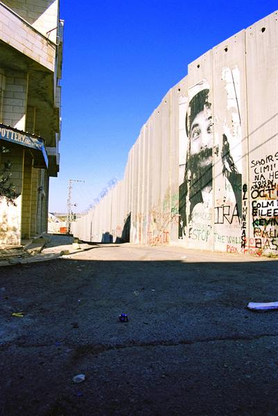 Concrete separation wall with mural poster along an empty sunlit street