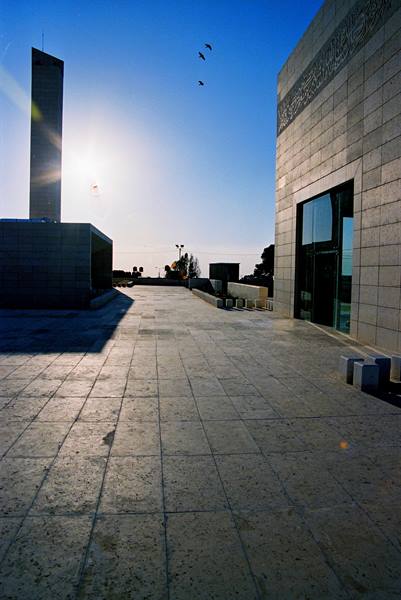 Stone-paved courtyard, slender minaret and low sun between two buildings