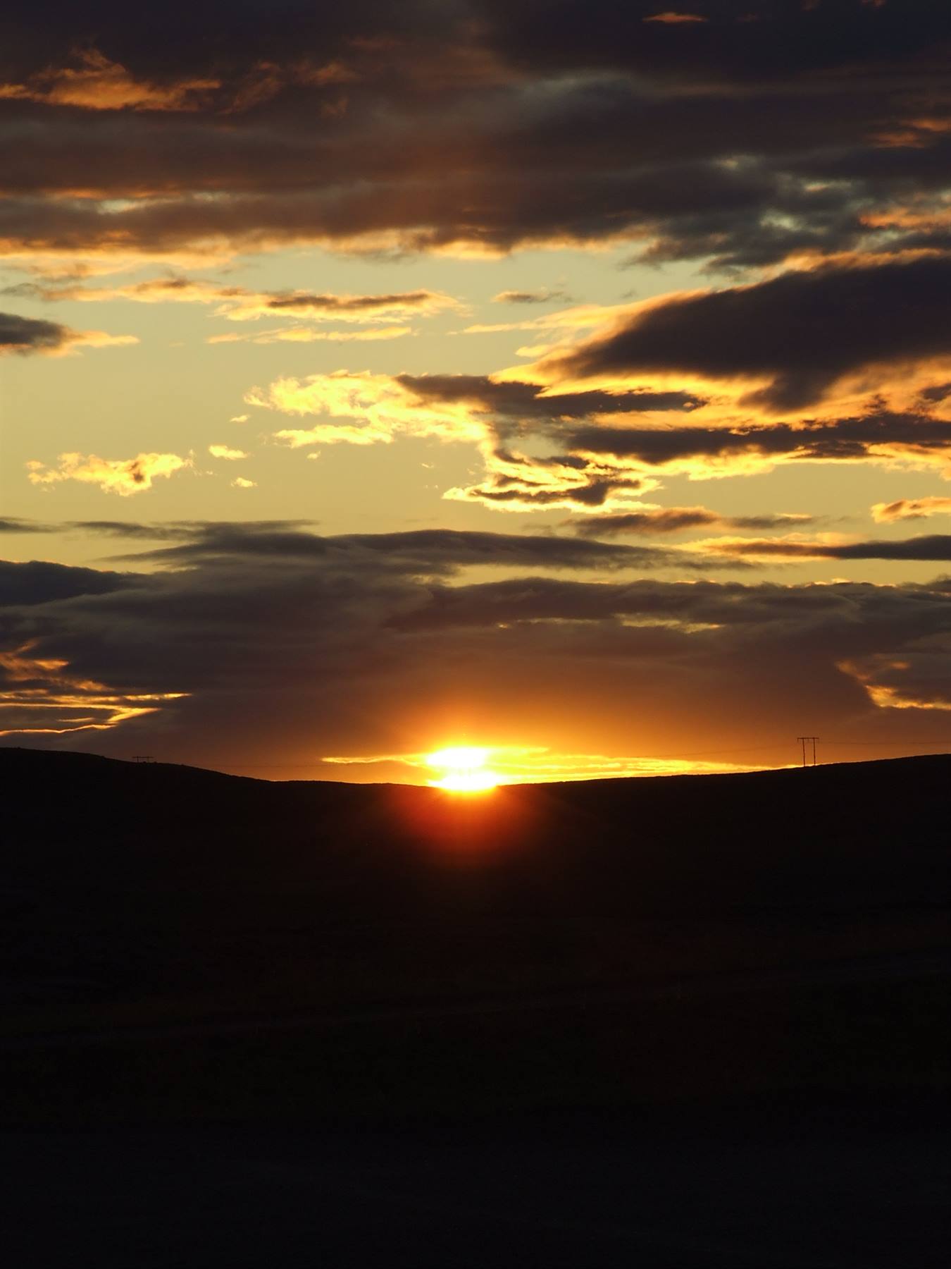 Low sun behind dark hills, golden clouds, power pylon on the ridge