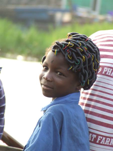Girl with colorful braided hair and blue shirt smiles among the crowd
