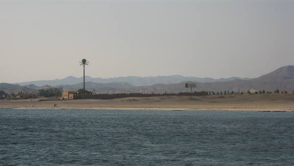Sandy beach with palm tree and houses, blue water and hazy mountains behind
