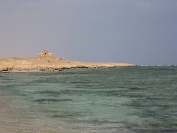 Turquoise waters before a sandy shore with an old stone church