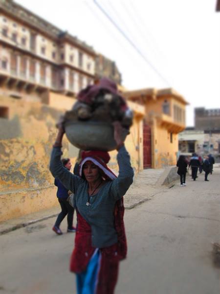 Woman in red sari carries a basin on her head near Amber's ochre walls
