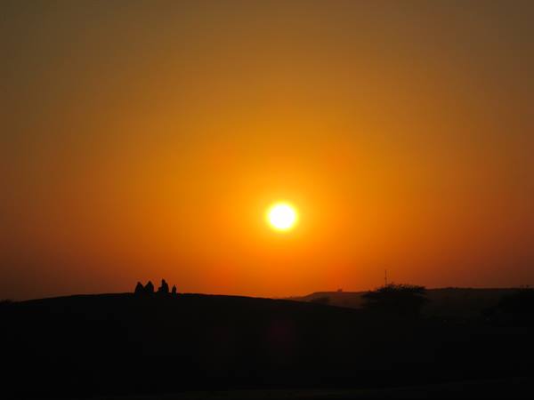 Low orange sun above dark hills, silhouetted figures standing on the ridge