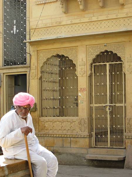 Man in pink turban sitting by carved sandstone facade, Jaisalmer