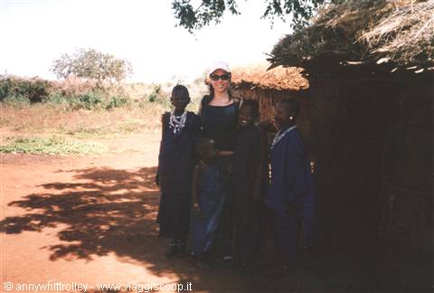 Tourist with Maasai children beside a mud and thatch hut