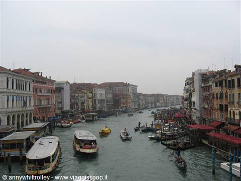 Vaporettos and boats on the Grand Canal between colorful buildings under grey sky