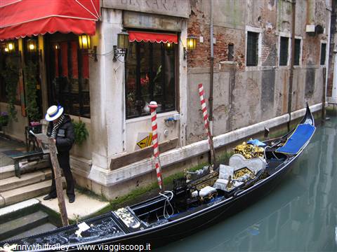 Black gondola moored beside a restaurant with a red awning in Venice
