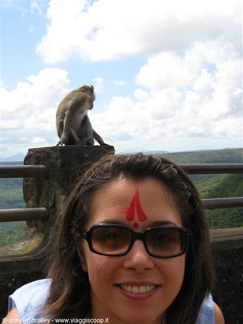 Woman with red tilaka and sunglasses, monkey sitting on stone wall behind
