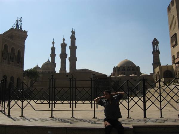 Man sitting by iron fences in Islamic Cairo, minarets and domes under sun