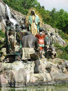Stone statues gathered before a golden Madonna statue on rocks with small waterfall