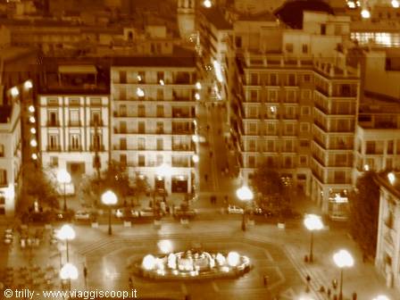 Night square with lit fountain, balconied buildings and glowing street lamps