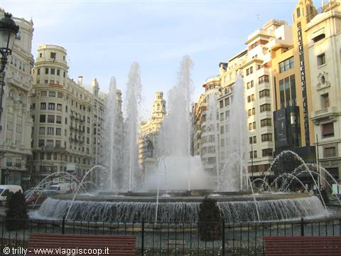Circular fountain with water jets surrounded by ornate buildings, Valencia