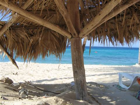Thatched wooden umbrella on white sand beach facing the turquoise sea