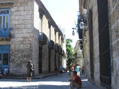 Pedestrians in Old Havana's colonial street lined with weathered stone buildings