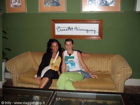 Two women sitting on a yellow sofa beneath Ernest Hemingway's framed signature