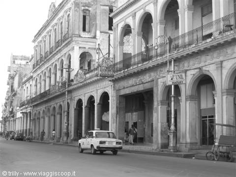 White vintage car parked by colonial arcade buildings, black and white