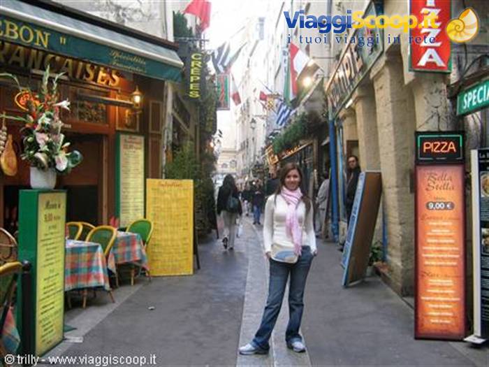 Smiling girl in a narrow Paris alley among creperies and pizza signs