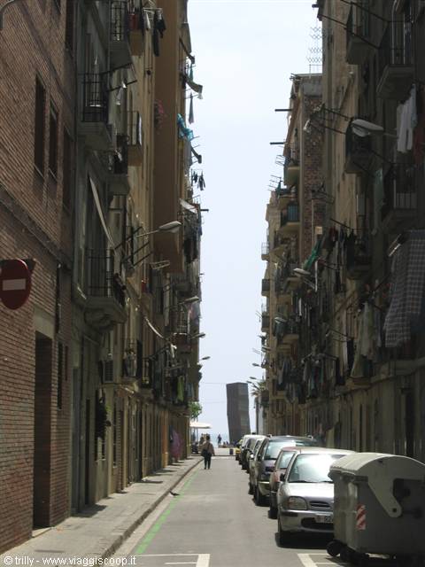 Barcelona alley with brick buildings, hanging laundry and cars toward the sea