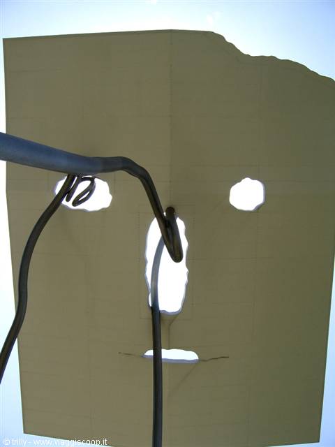 Metal face sculpture with curved pipe, backlit sky