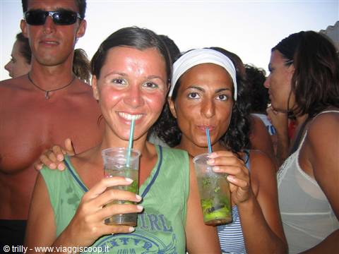 Two smiling girls sipping mojitos with straws, crowd around