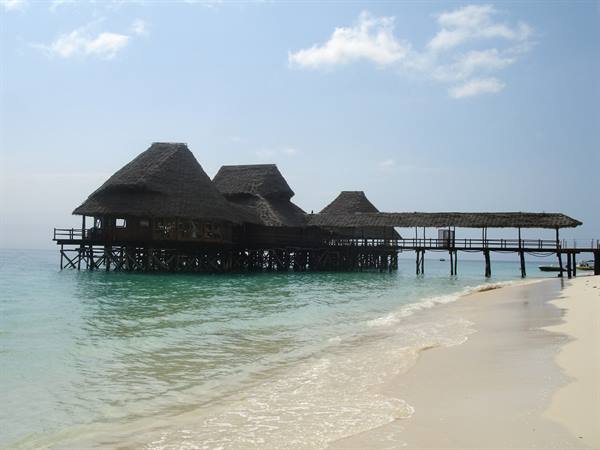 Stilt bar with thatched roofs over turquoise water, white sand beach