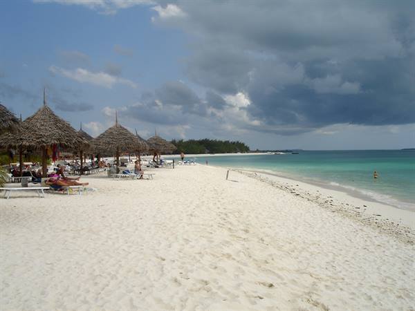 White sand beach with thatched umbrellas and tourists, cloudy sky