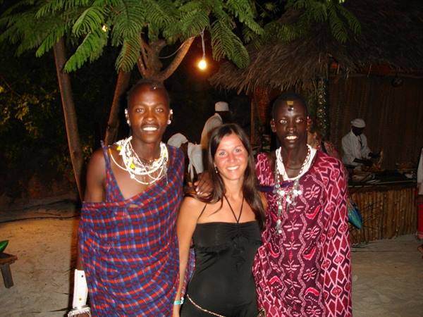 Tourist in black dress with two Maasai men in red shukas, beach at night