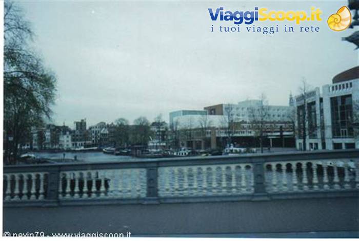 Amsterdam canal seen from stone bridge, houses and Stopera building under grey sky