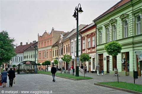 Pedestrians stroll past colorful historic facades along a pedestrian street with lampposts