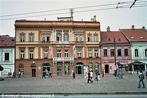 Pedestrians crossing a square in front of a yellow Volksbank building and colorful facades