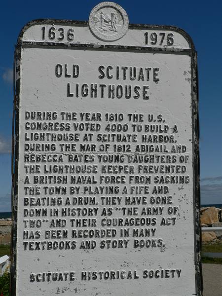 White historical marker of Old Scituate Lighthouse with sea and rocks behind