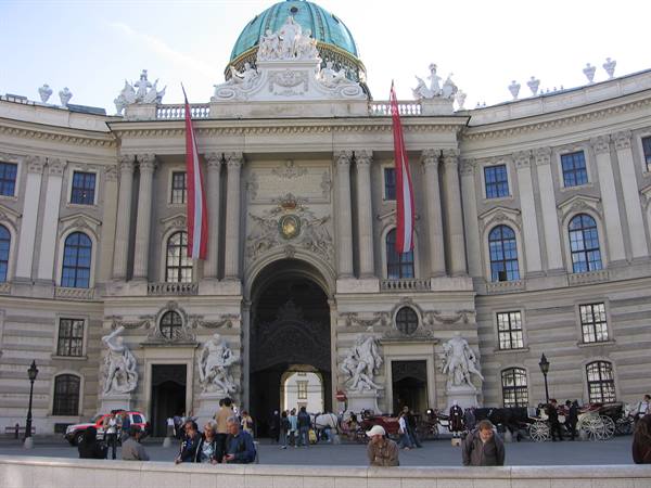 Baroque facade of the Hofburg in Vienna with red flags and horses