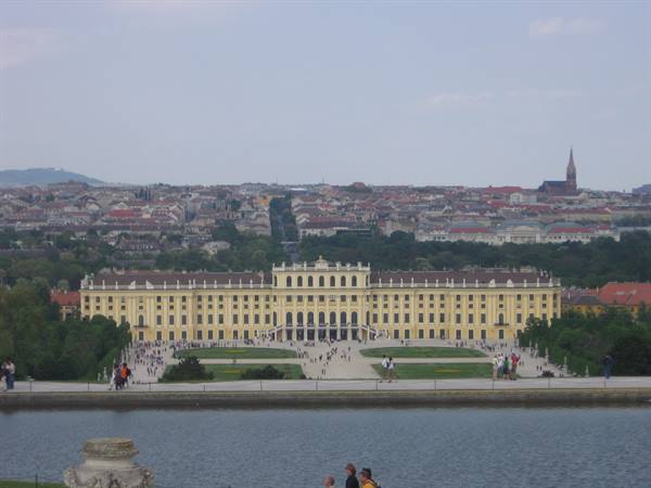 Tourists stroll in the gardens in front of yellow Schönbrunn Palace