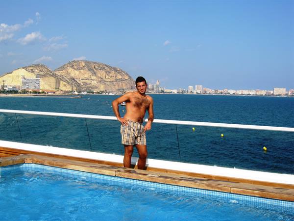 Man in swim shorts by ship pool, Alicante waterfront in background