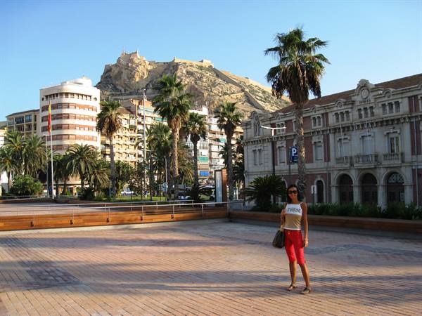 Tourist in red trousers on paved square, Santa Bárbara castle above Alicante