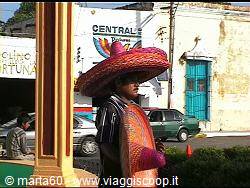 Man wearing a colorful straw sombrero beside a pole near buildings