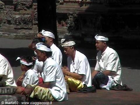 Men in white with headbands pray sitting on the ground at a Balinese temple