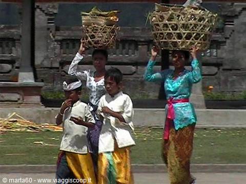 Women carrying woven baskets on heads with children in traditional Balinese dress