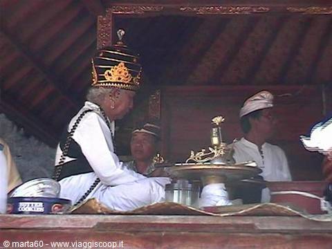 Balinese priest in golden crown performing a temple ritual with incense and offerings