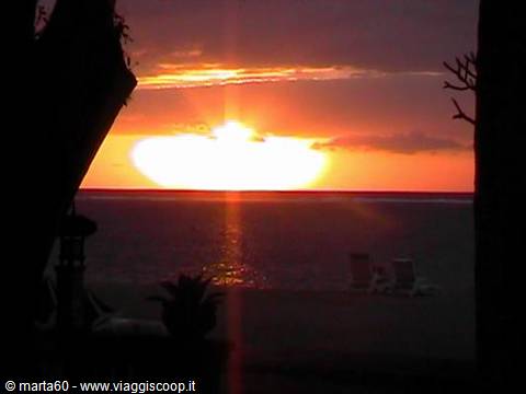 Sun sinking into the ocean behind two beach loungers