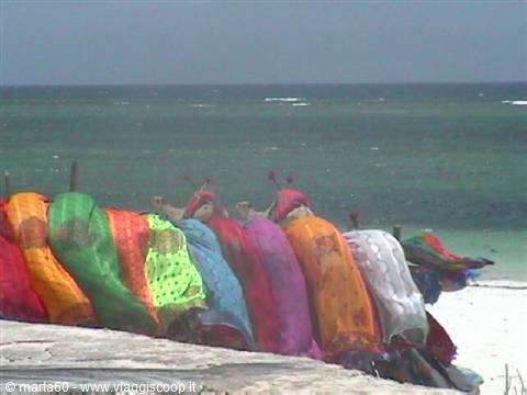 Women in colorful clothes and turbans sell fabrics on the white beach