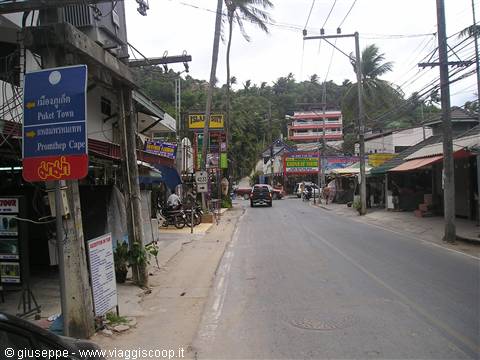 Road with signs to Patong Town and Promthep Cape, palm trees and shops, overcast light
