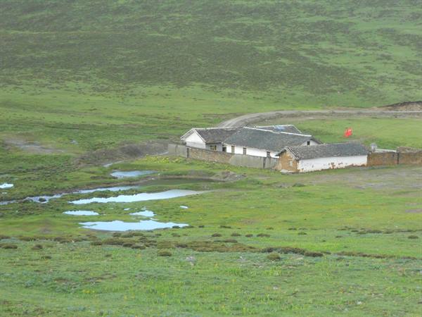 Rural white-walled house with dark roof in green meadow with ponds